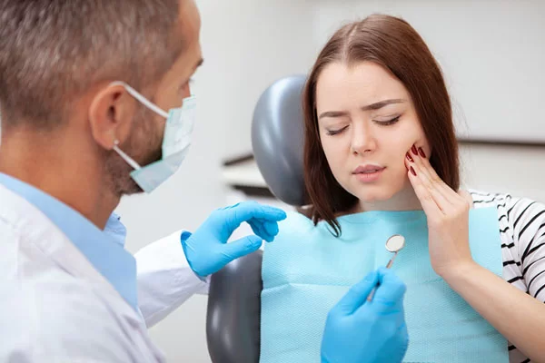 patient holding her cheeks as the dentist lift up dental tools to look into the dental pain